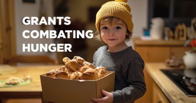 Small boy with curly blonde hair poking out from beneath his cap. He's holding a box of food.